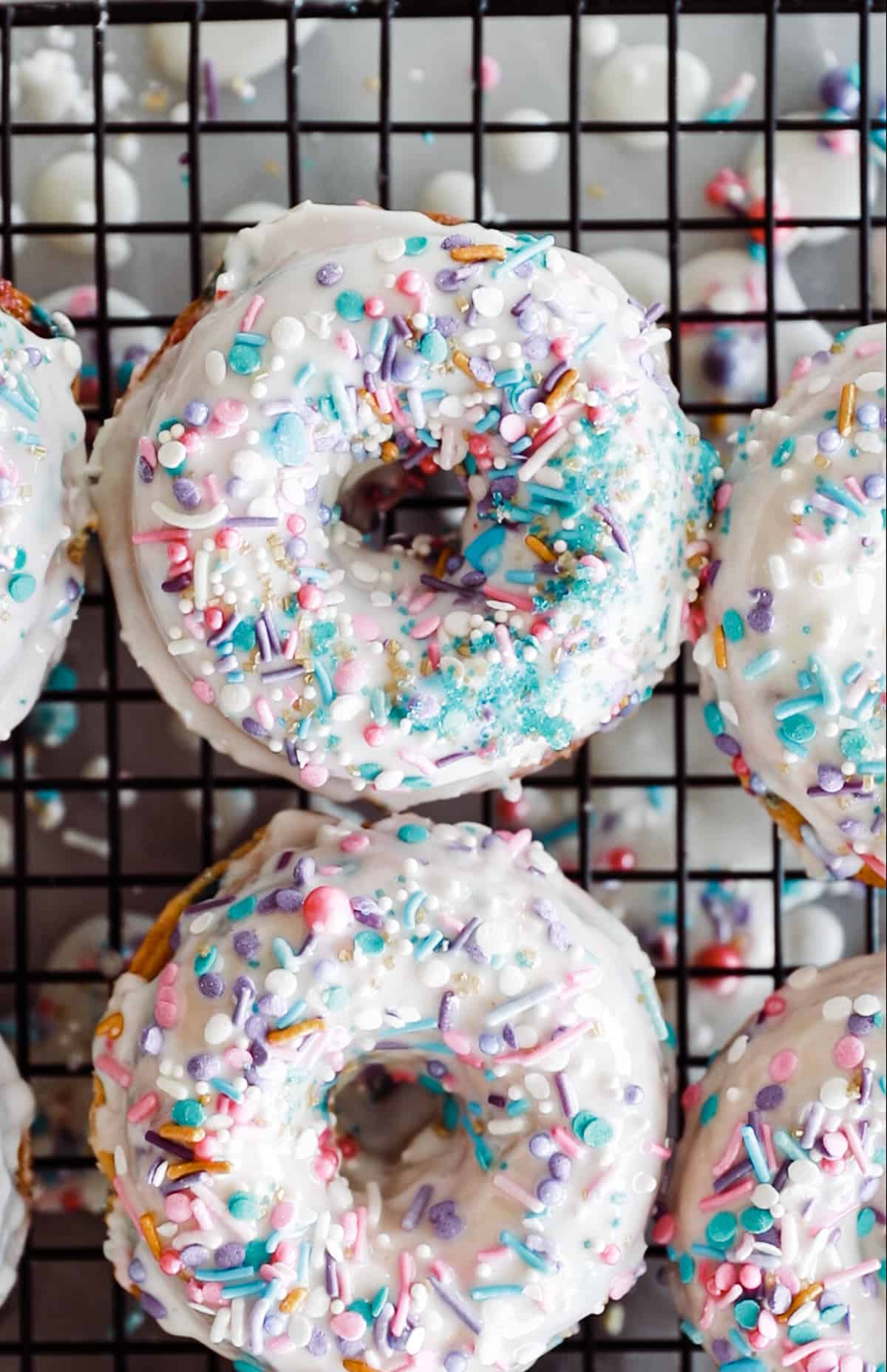 Frosted and sprinkled donuts on a cooling rack. 