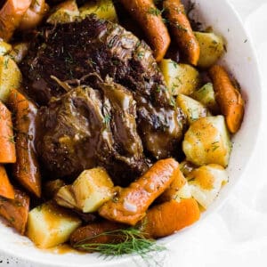 Frozen roast beef in a bowl surrounded by carrots and potatoes.