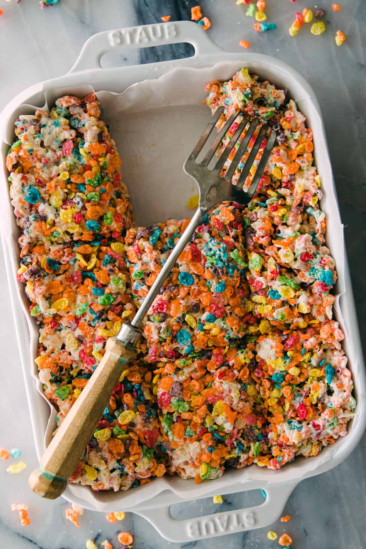 white pan with rainbow fruity pebble Krispie treats and a large serving fork 
