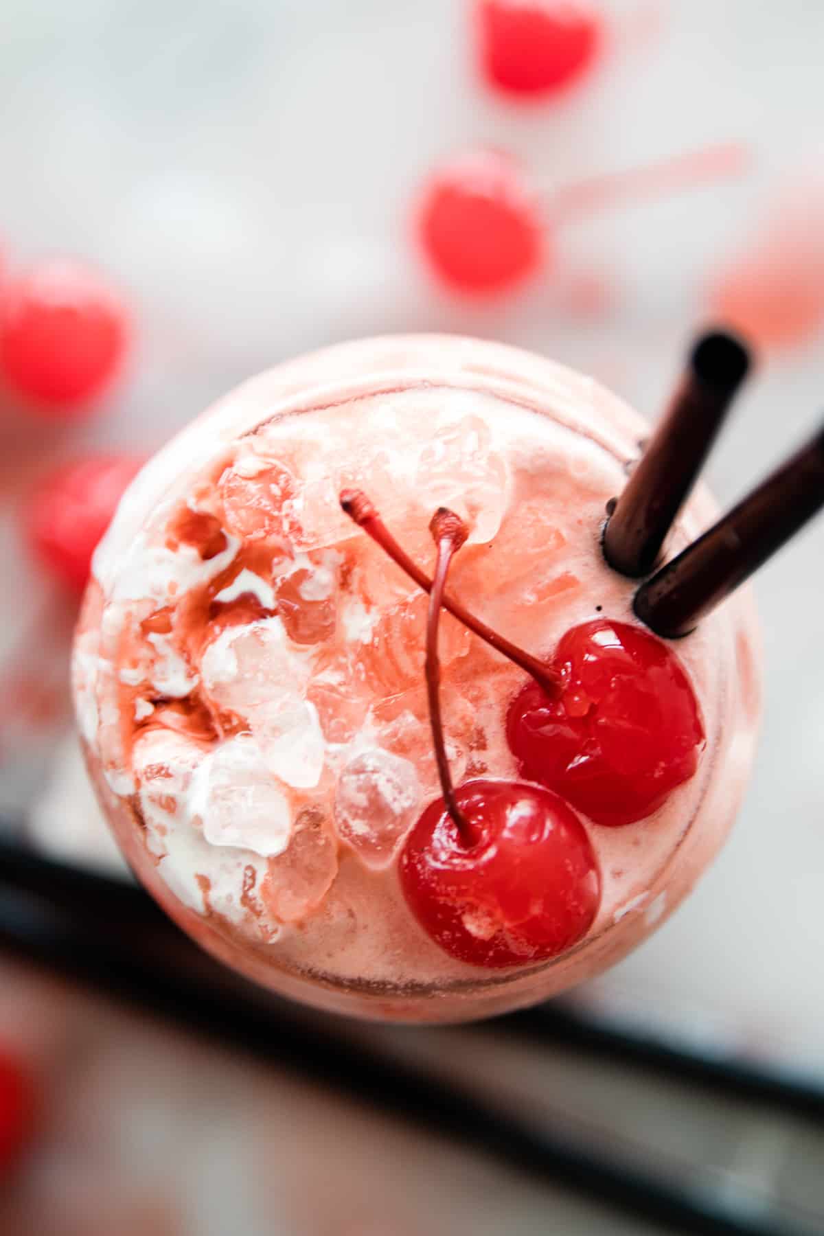 photo of a cup from the top with two cherries, two straws and a creamy ice pink liquid of Italian soda