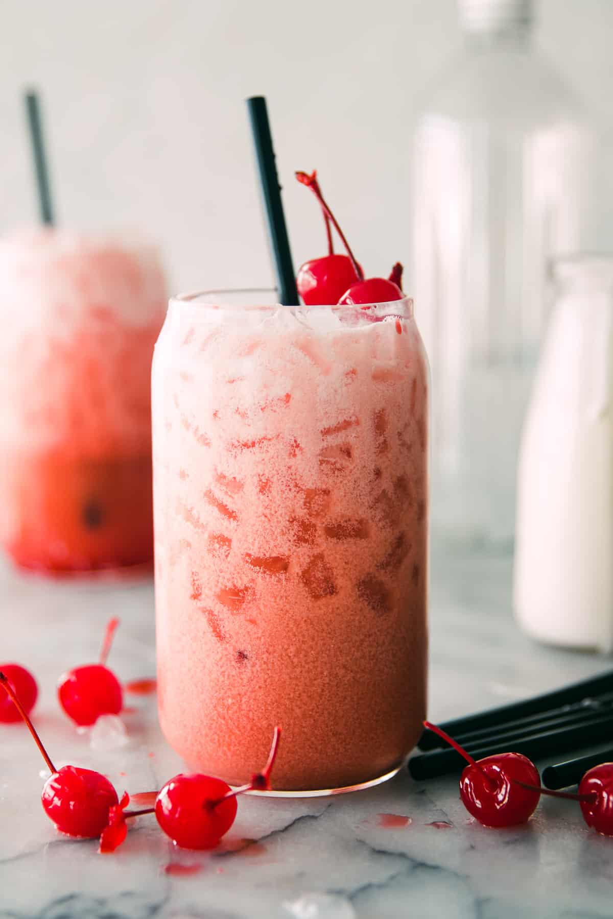 one creamy pink drink with ice and two cherries on top and. black straw. 