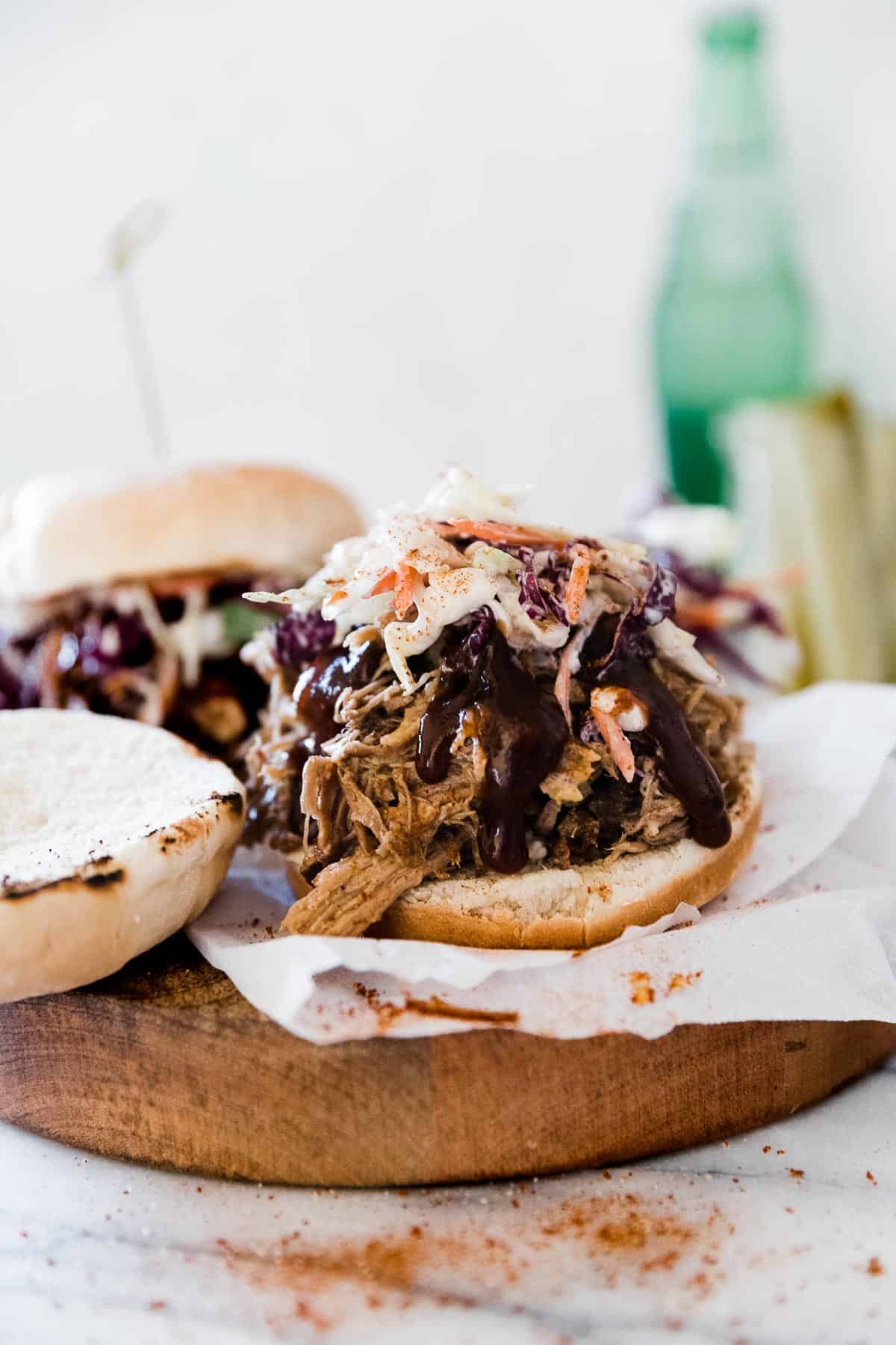 Pulled pork on a bun, topped with slaw and bbq sauce. There is a jar of pickles in the background.