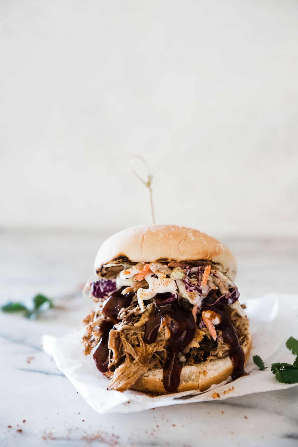 A close up of a pressure cooker pulled pork sandwich on a piece of parchment paper.