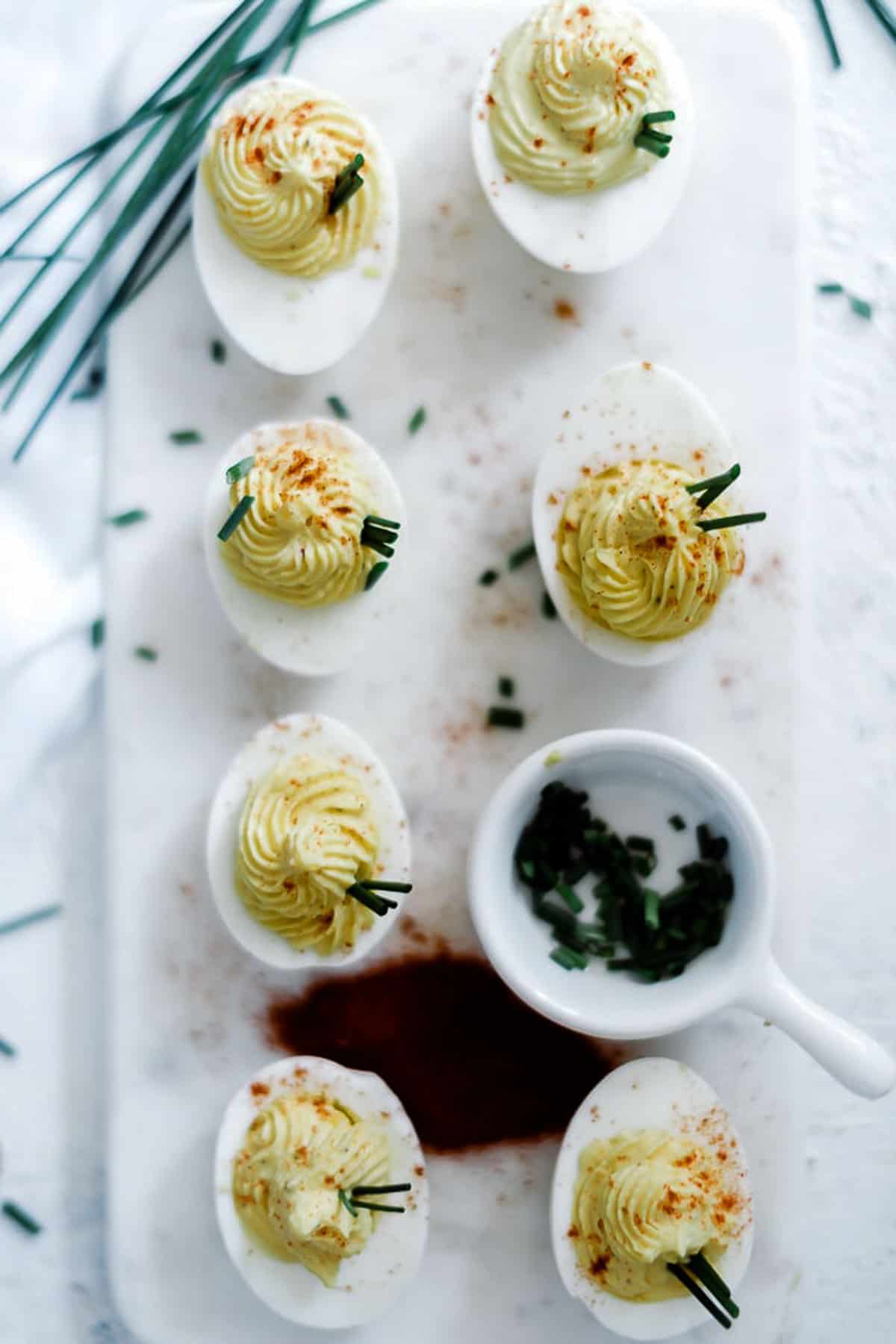 5 star deviled egg recipe on a marble tray. There is a small bowl of chives to the side.