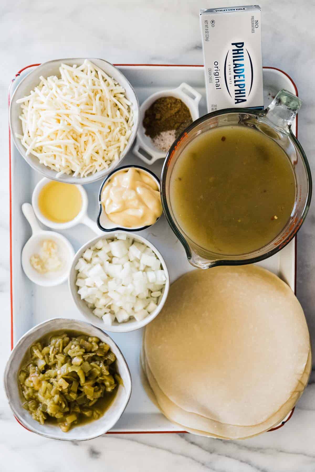 Ingredients needed for chicken enchiladas on a white baking sheet.