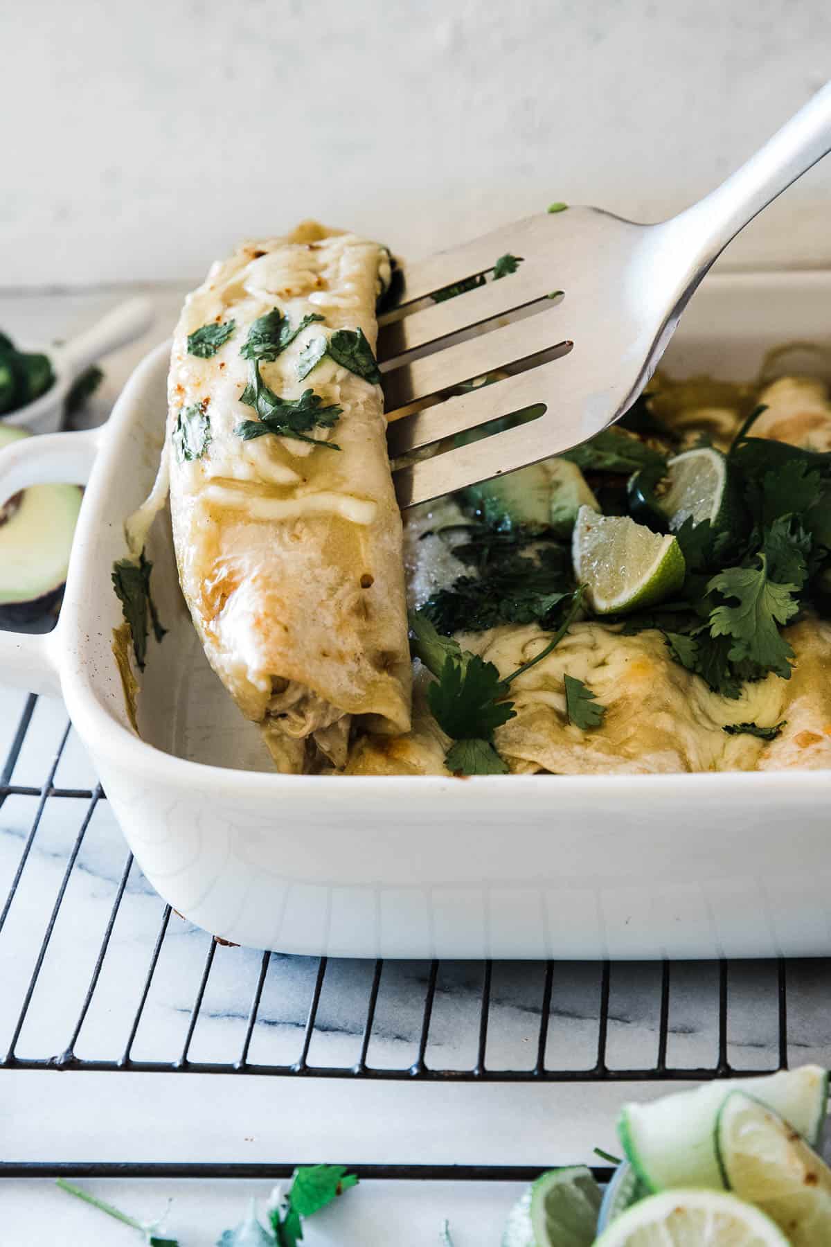 Chicken enchiladas being lifted out of a pan with a metal spatula.