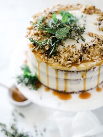 Carrot cake recipe from scratch on a marble cake plate. The cake is garnished with caramel and walnuts.