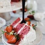 A large slice of strawberry coconut cake on a white dessert plate. There is a black fork stuck into the slice.