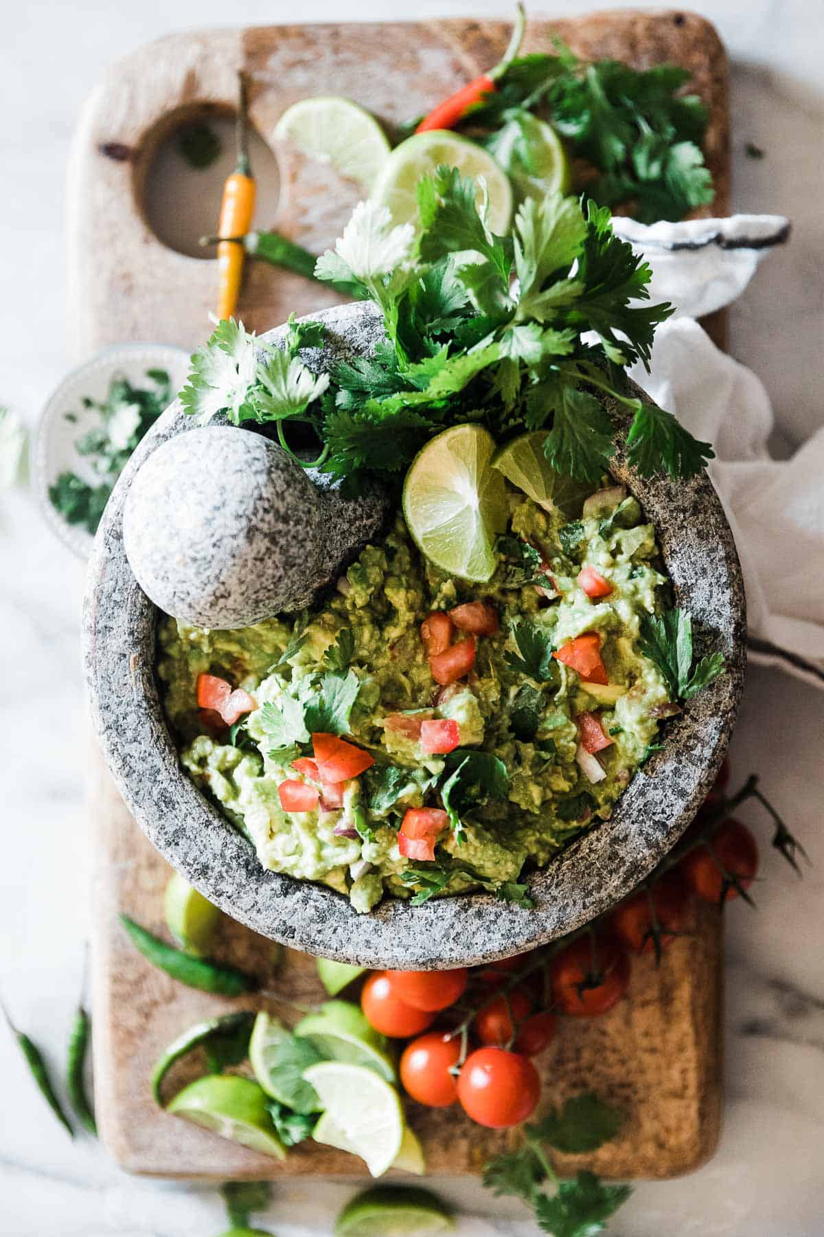 Homemade guacamole recipe in a grey bowl, garnished with cilantro. There are peppers surrounding the bowl.