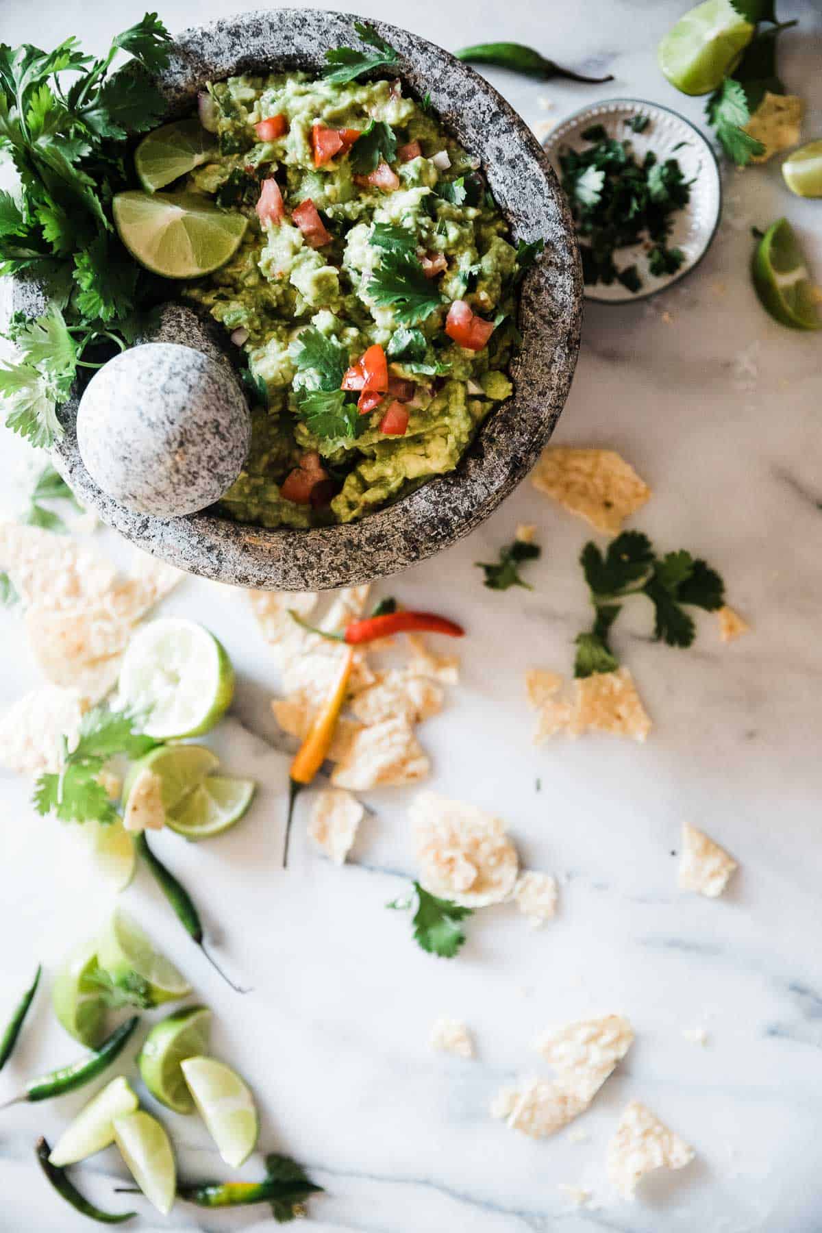 Homemade guacamole recipe in a grey bowl. It is surrounded by chips and peppers.