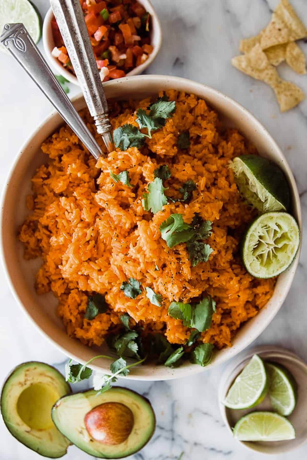 A big bowl of red Mexican rice with limes and cilantro as garnish