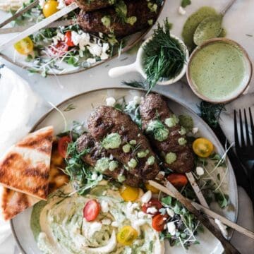 Kofta kebab recipe on plates that are smeared with hummus and green goddess dressing.