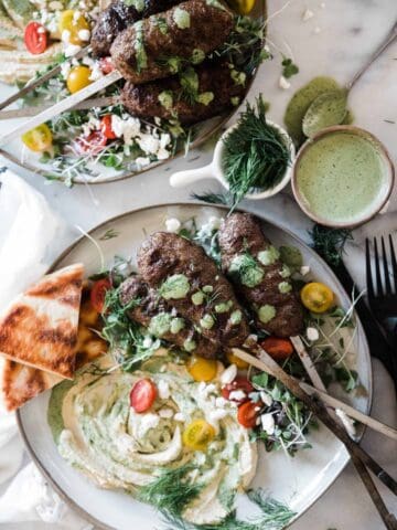 Kofta kebab recipe on plates that are smeared with hummus and green goddess dressing.