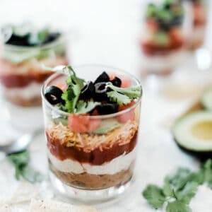 Layered taco dip in a small glass. There are two more set behind.