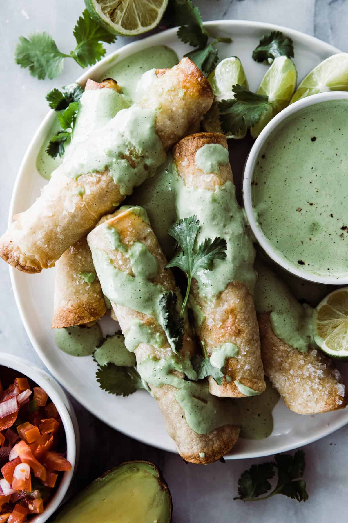 Cripsy Chicken taquitos on a plate with a creamy cilantro dressing on the side. 