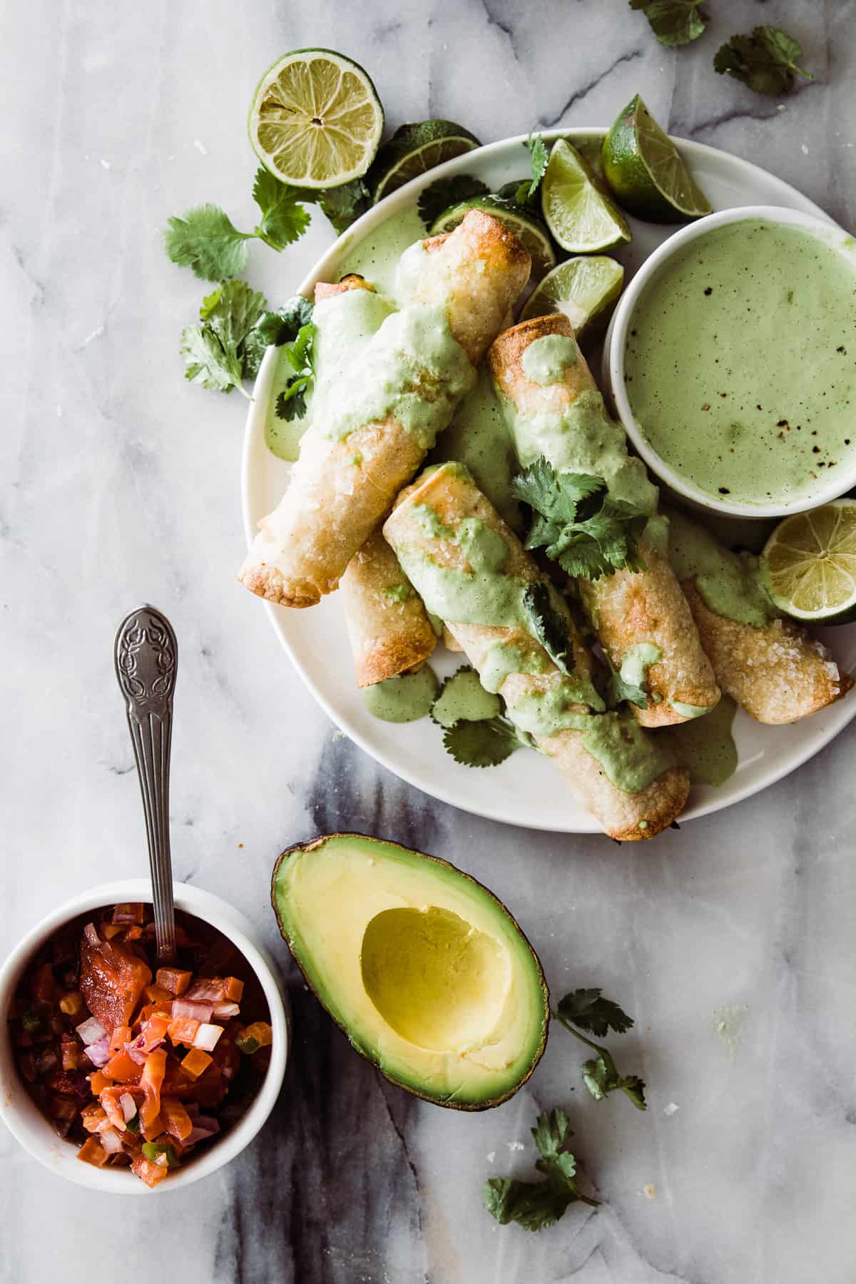 Cripsy Chicken taquitos on a plate with a creamy cilantro dressing on the side with avocado and pico de gallo. 