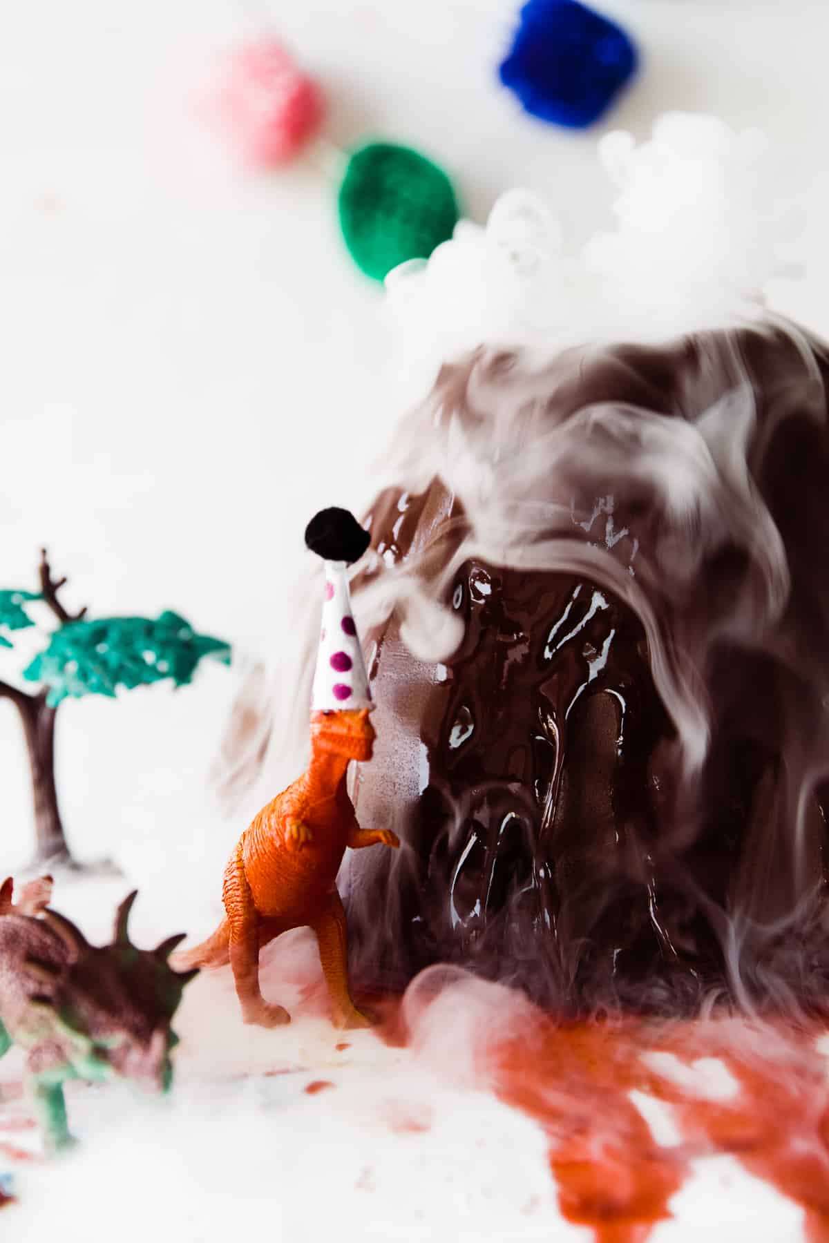 dinosaur with party hat on cake next to smoking volcano