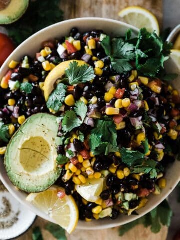An overhead shot of cowboy caviar recipe in a white bowl. It is garnished with avocado and lemon wedges.
