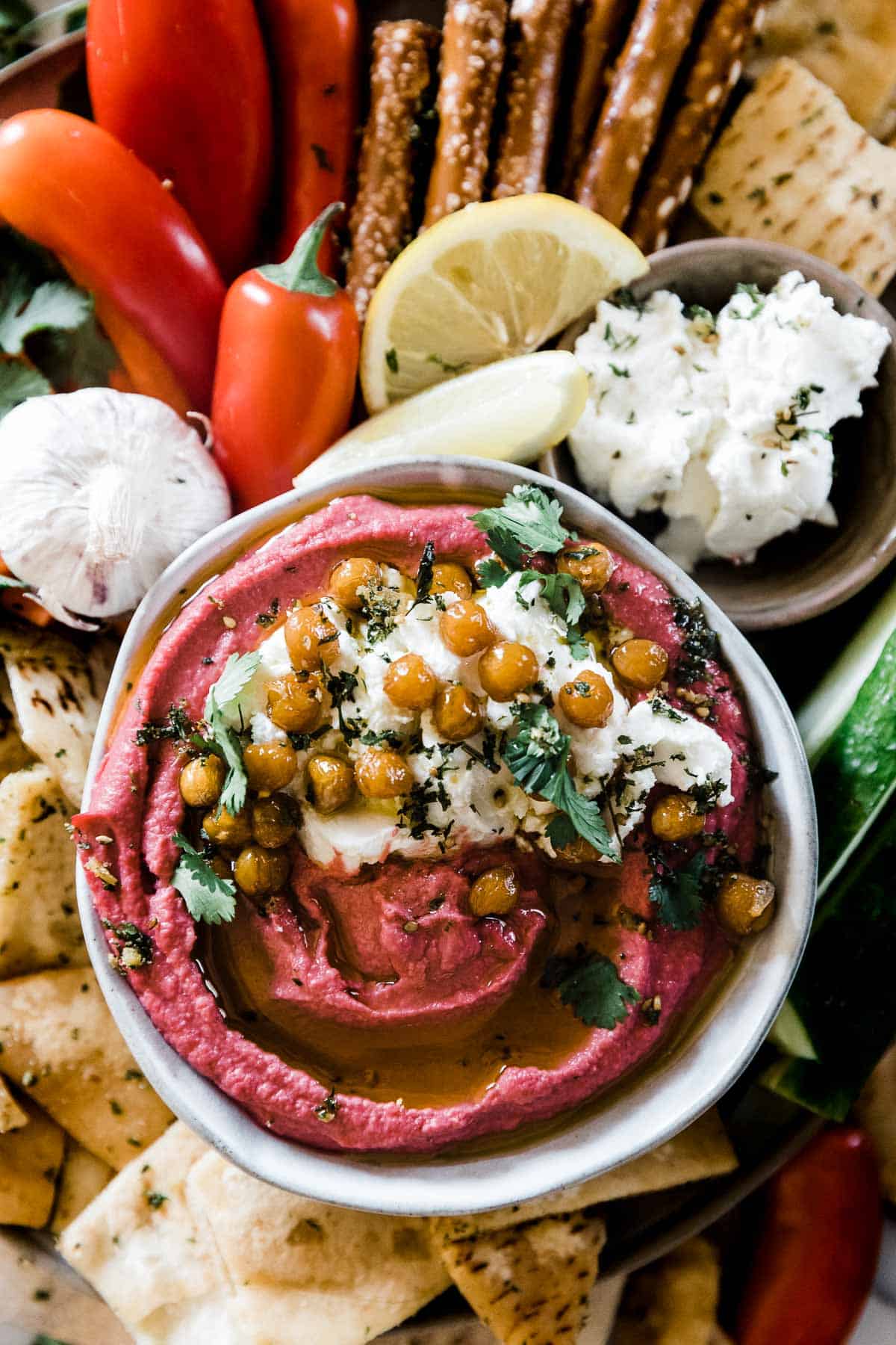 An overhead shot of beet hummus on a serving platter surrounded by veggies and pita chips.