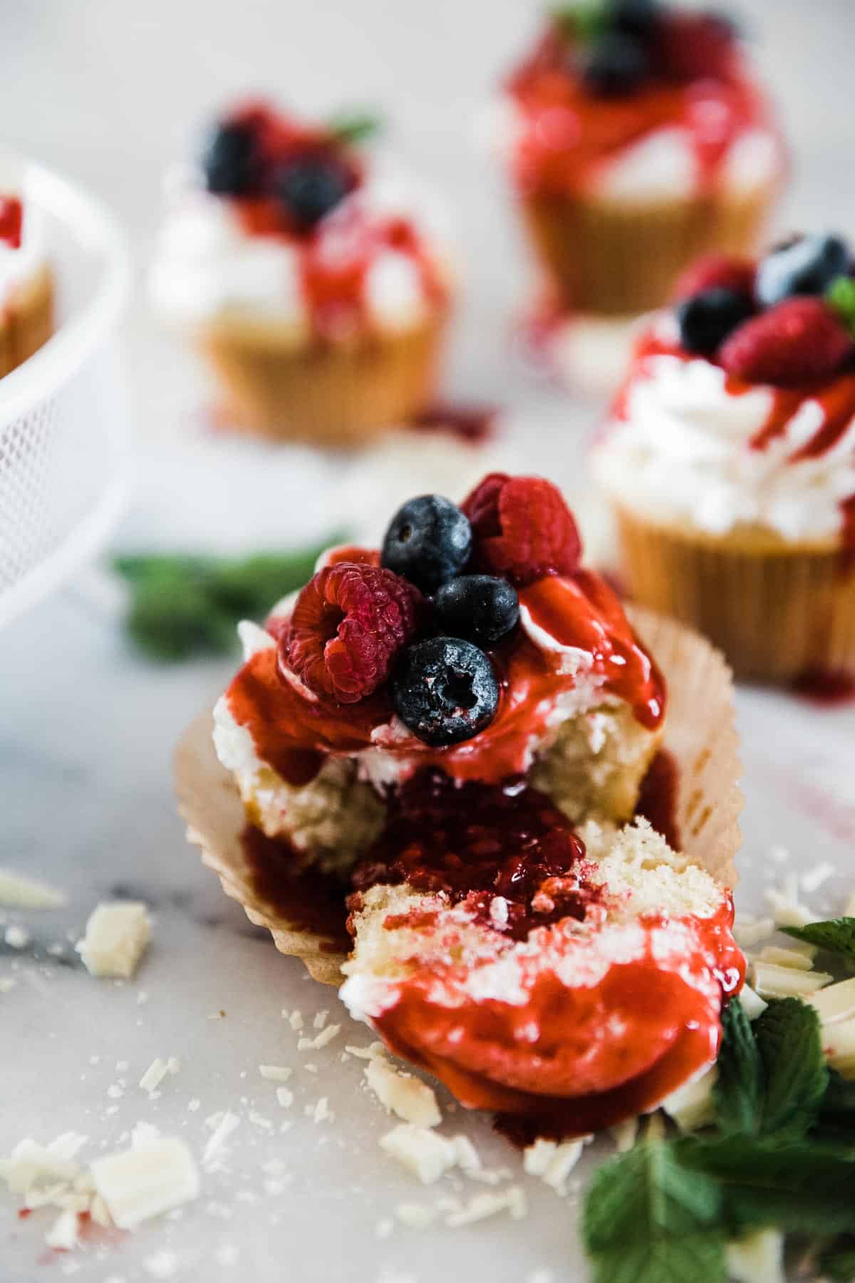 A closeup of a white chocolate raspberry cupcake cut in half and garnished with berries.