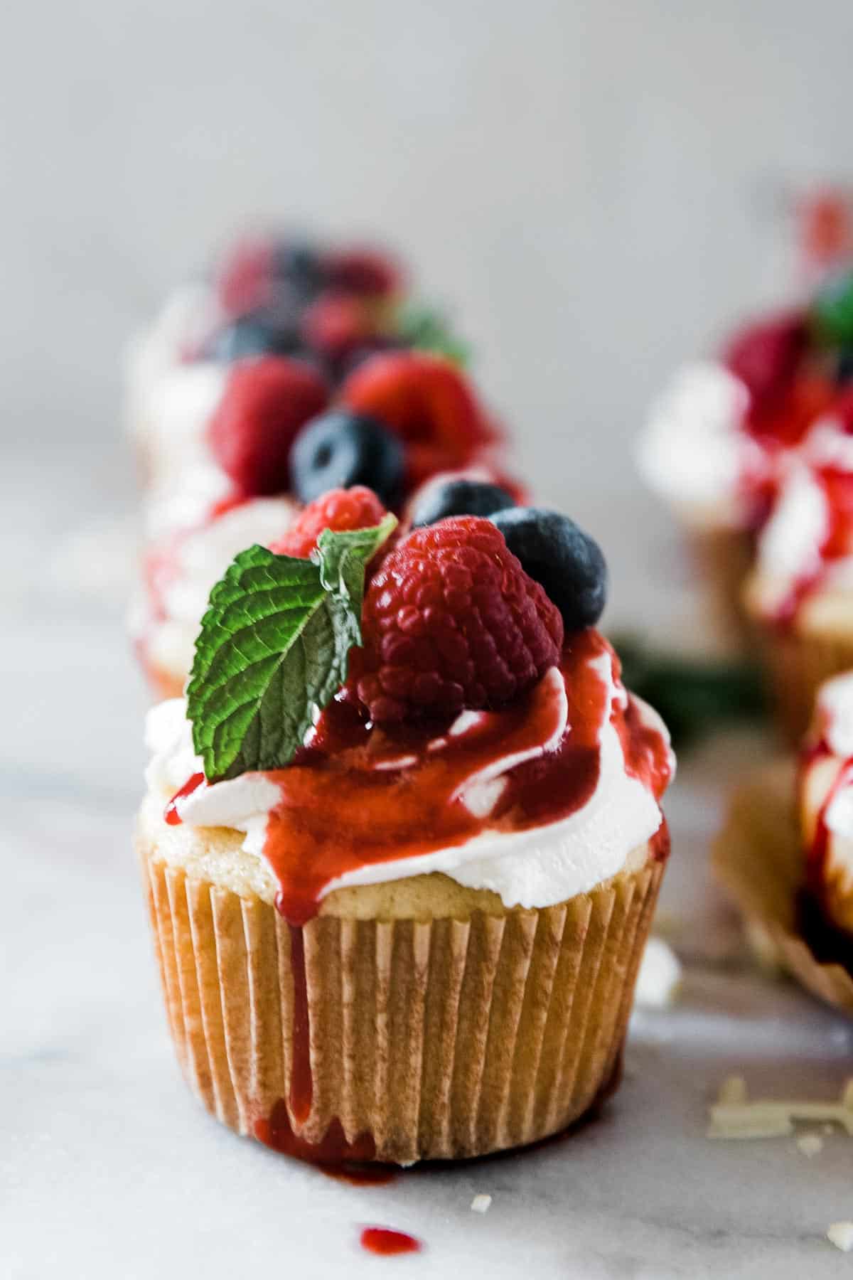A close up of white chocolate raspberry cupcake garnished with berries and mint.