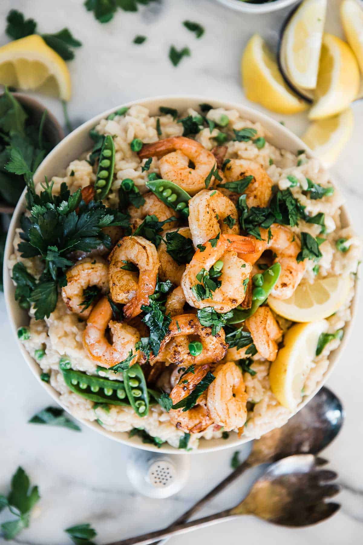 Shrimp risotto recipe in a white bowl. There are jumbo shrimp piled high, and it is garnished with parsley.