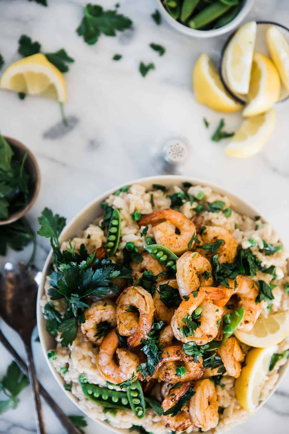 Shrimp risotto recipe in a white bowl atop a marble counter. There are lemons to the side.