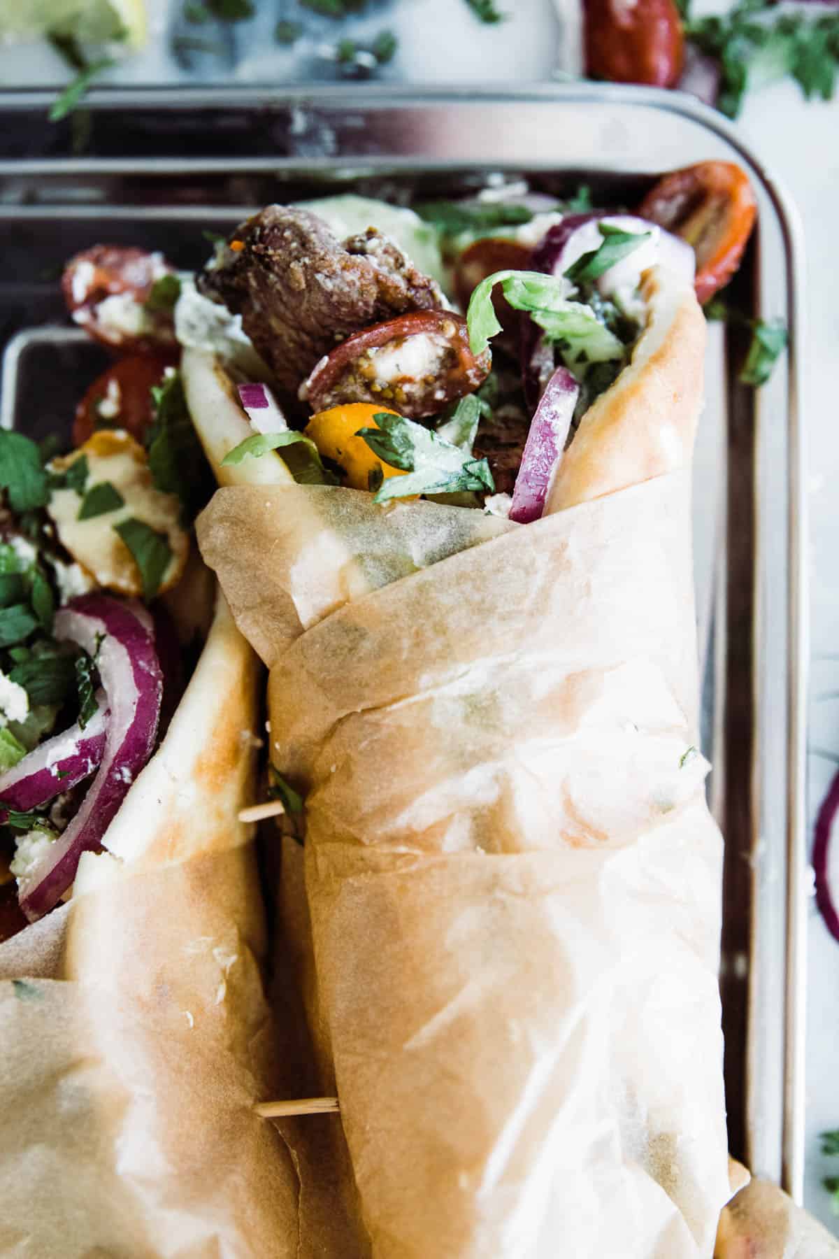 two lamb gyros wrapped in brown paper served on a tray.
