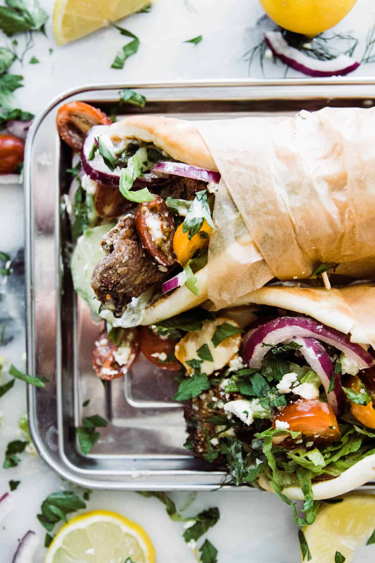 Two lamb gyros wrapped in brown paper served on a tray.