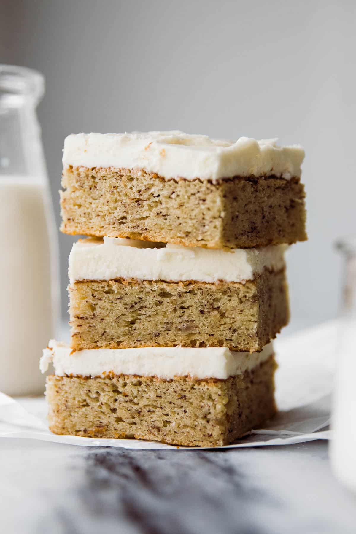 Three fluffy banana bars stacked on top of each other frosted with cream cheese frosting.