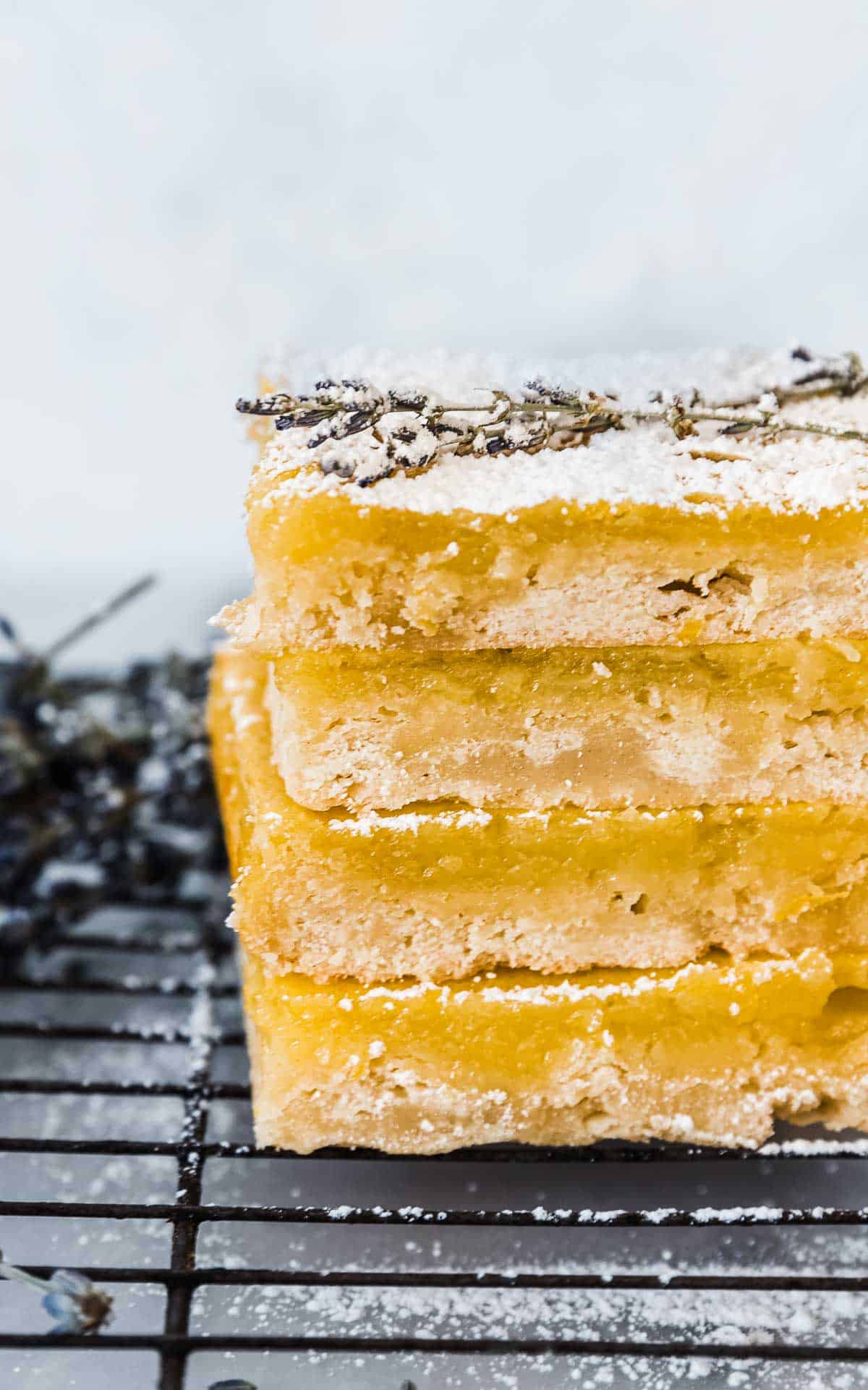 Three lemon bars stacked atop a wire cooling rack. The bars are garnished with powdered sugar and lavender.