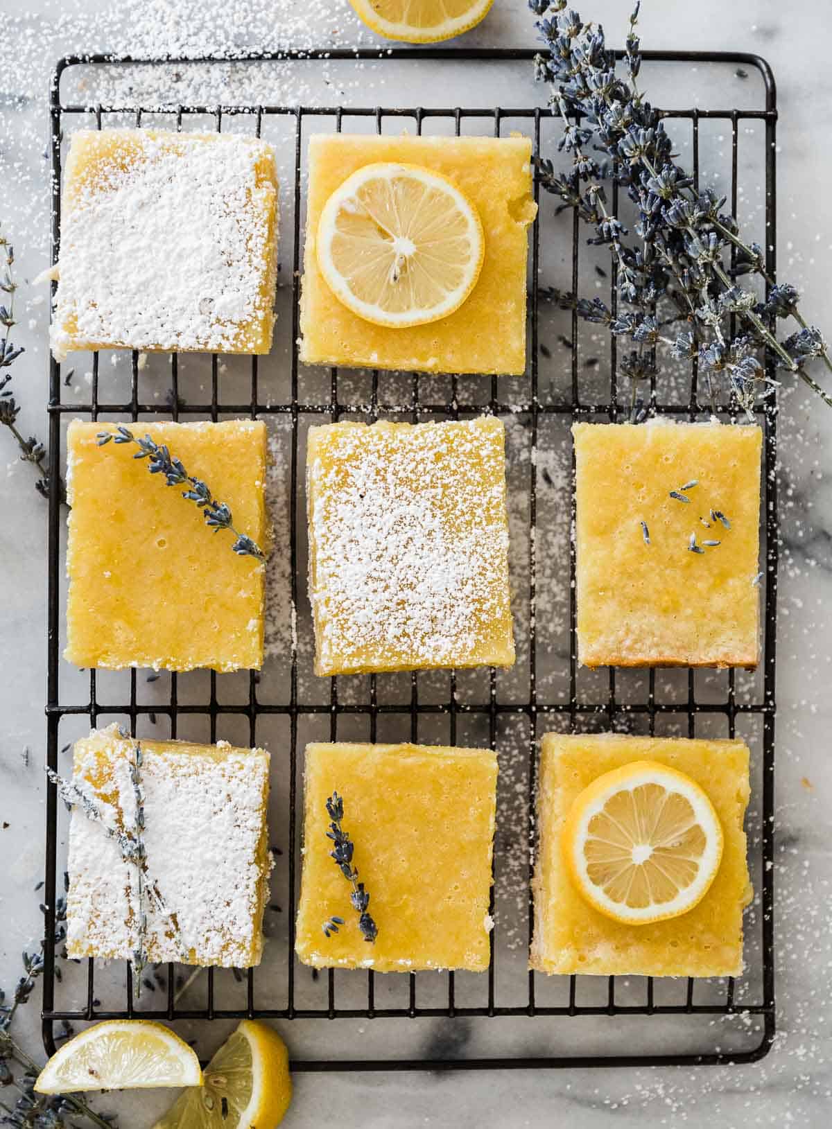 Easy lemon bars laid out on a wire cooling rack. They are garnished with lemon slices, and lavender sprigs.