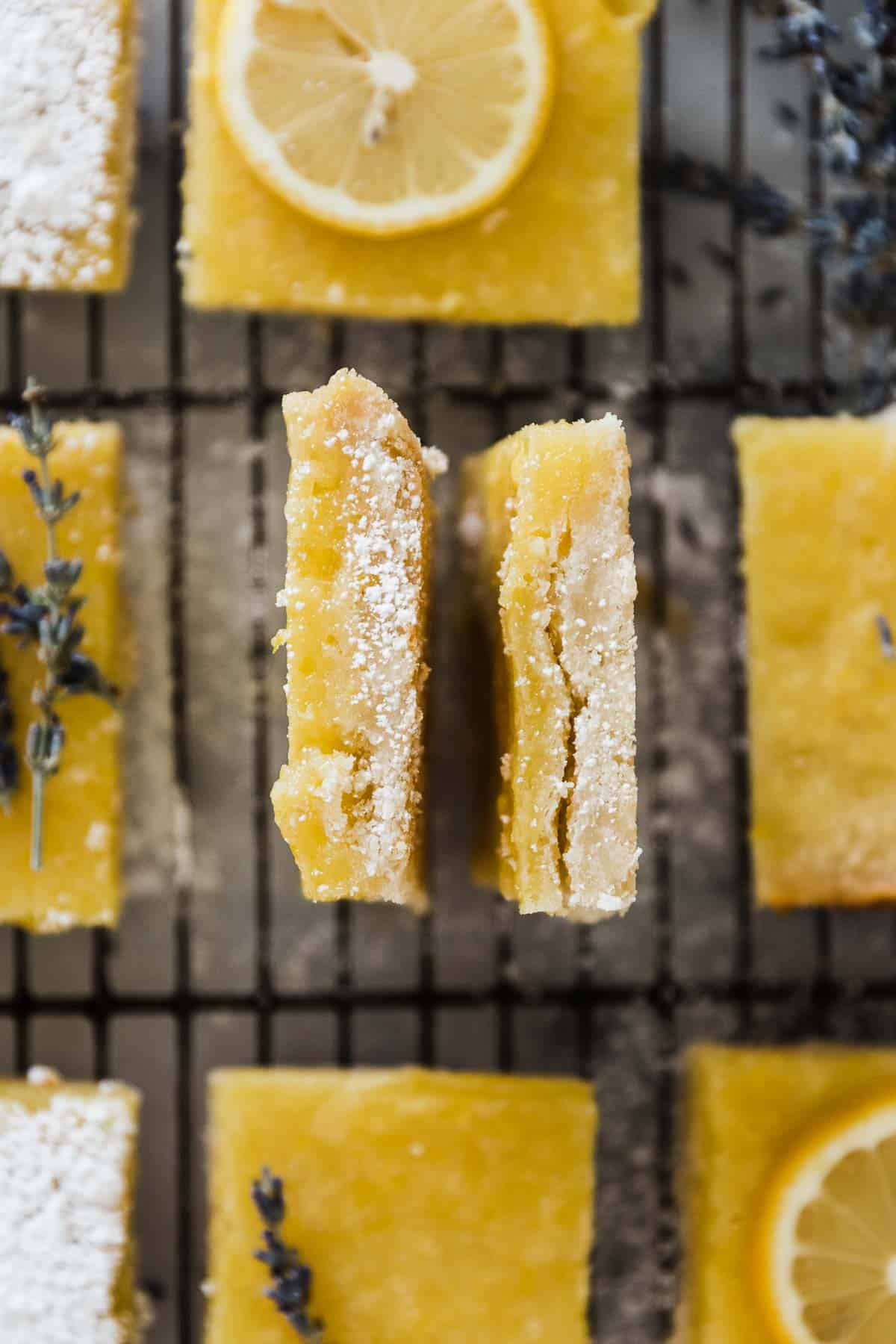 A closeup of two easy lemon bars laid on their sides to show the layers. They are surrounded by other lemon squares.
