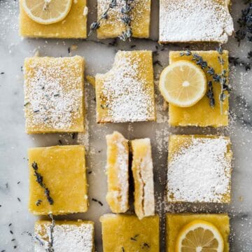 Easy lemon bars, sliced into squares and laid on a marble counter. There are a few garnished with lemon slices, lavender, and powdered sugar.