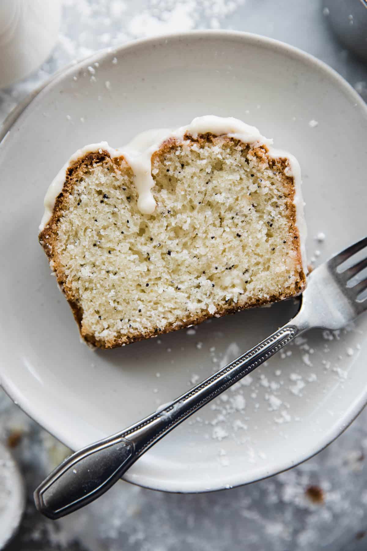 One slice of poppy seed bread with lemon glaze on a plate with fork. 