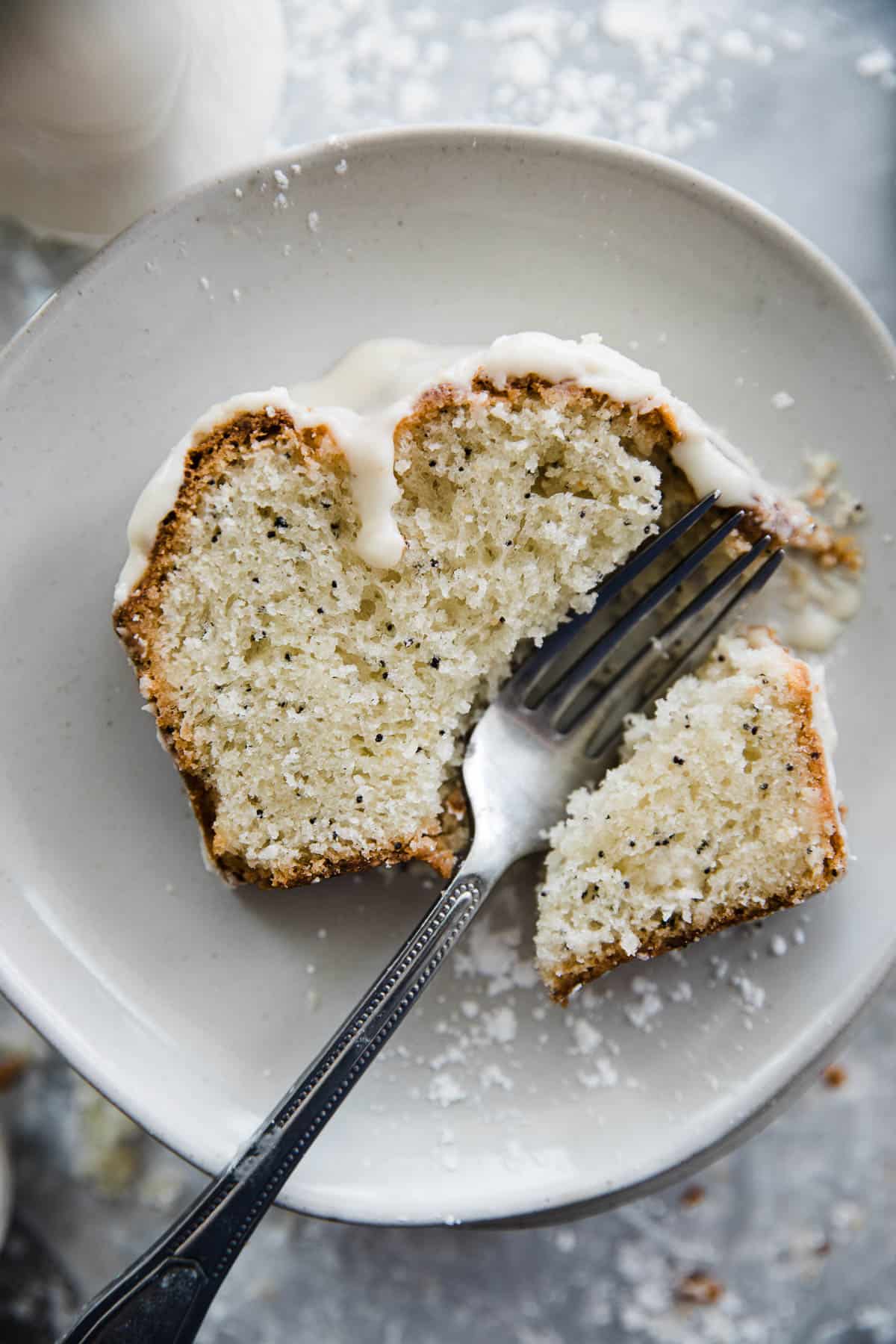 One slice of poppy seed bread with glaze and a fork cutting into the slice on the plate. 