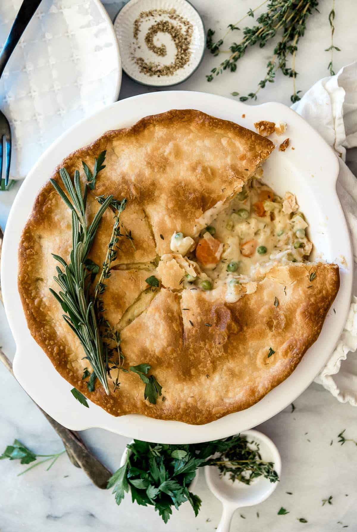 An overhead shot of pot pie recipe in a white pie plate. There are herbs to the side.