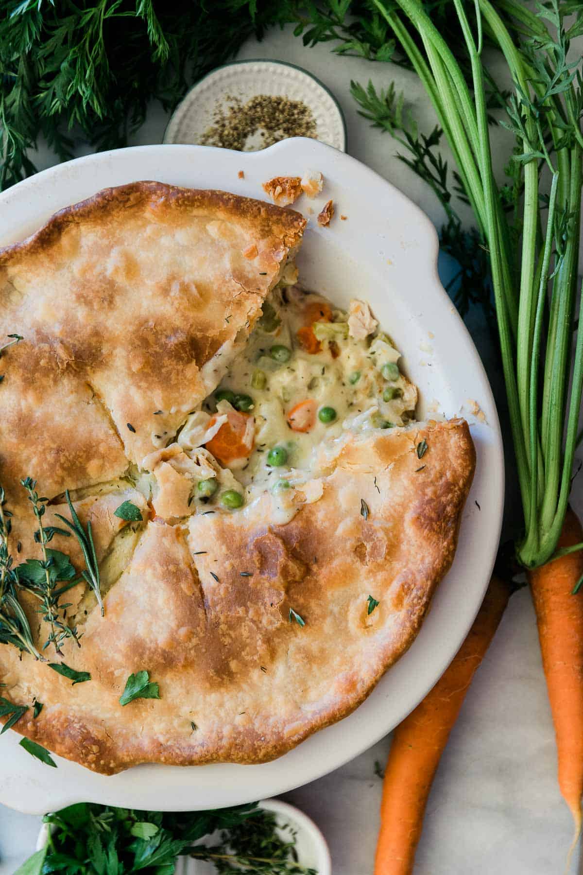 Pot pie recipe in a white pie pan. There are carrots to the side.