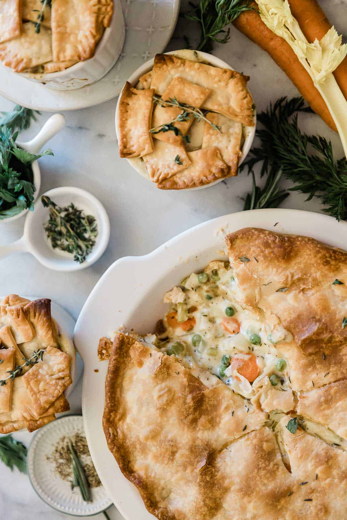 A large pot pie on a marble counter surrounded by mini pot pies and herbs.