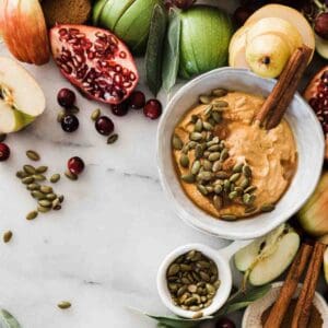 Pumpkin dip recipe in a bowl surrounded by fruit and garnished with cinnamon sticks
