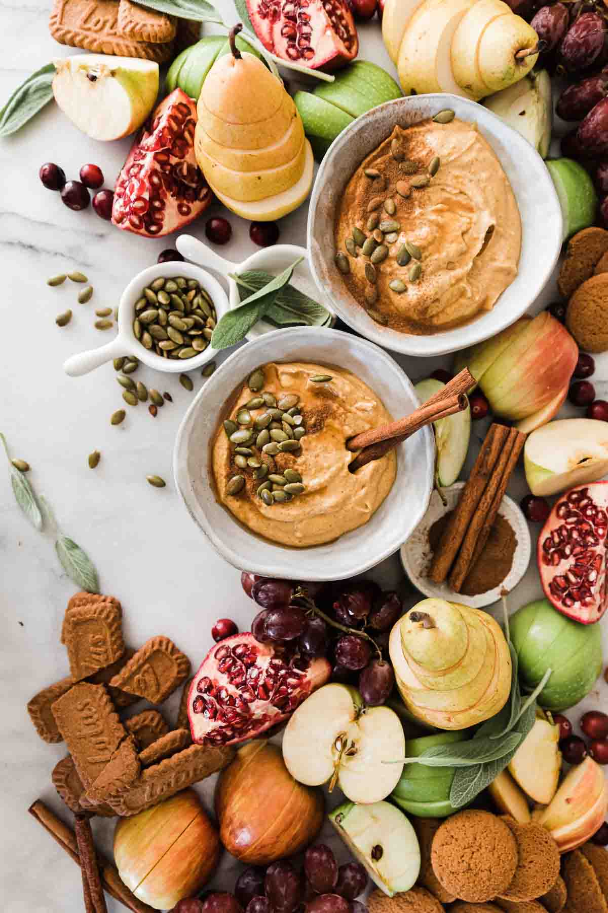 Two bowl of pumpkin dip recipe garnished with pipits. They are surrounded by fruit and cookies.