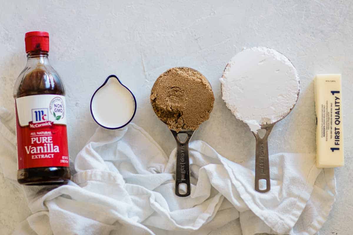 Vanilla, milk, brown sugar, powdered sugar, and butter on a white counter.