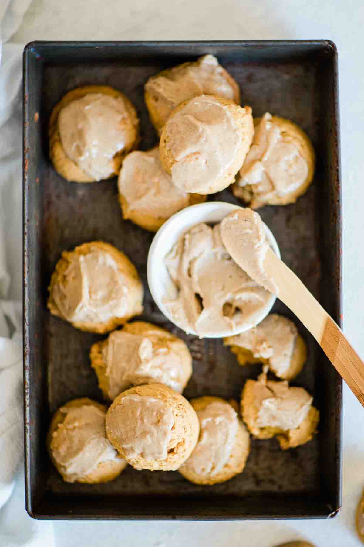 Soft pumpkin cookies in a metal pan. There is a bowl of frosting in the middle.