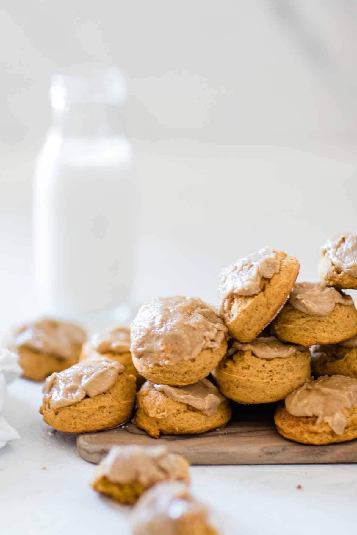 Soft pumpkin cookies on a wooden board. There is a bottle of milk in the background.
