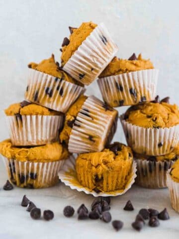 Easy pumpkin muffins stacked into a pyramid. There are chocolate chips spread around.