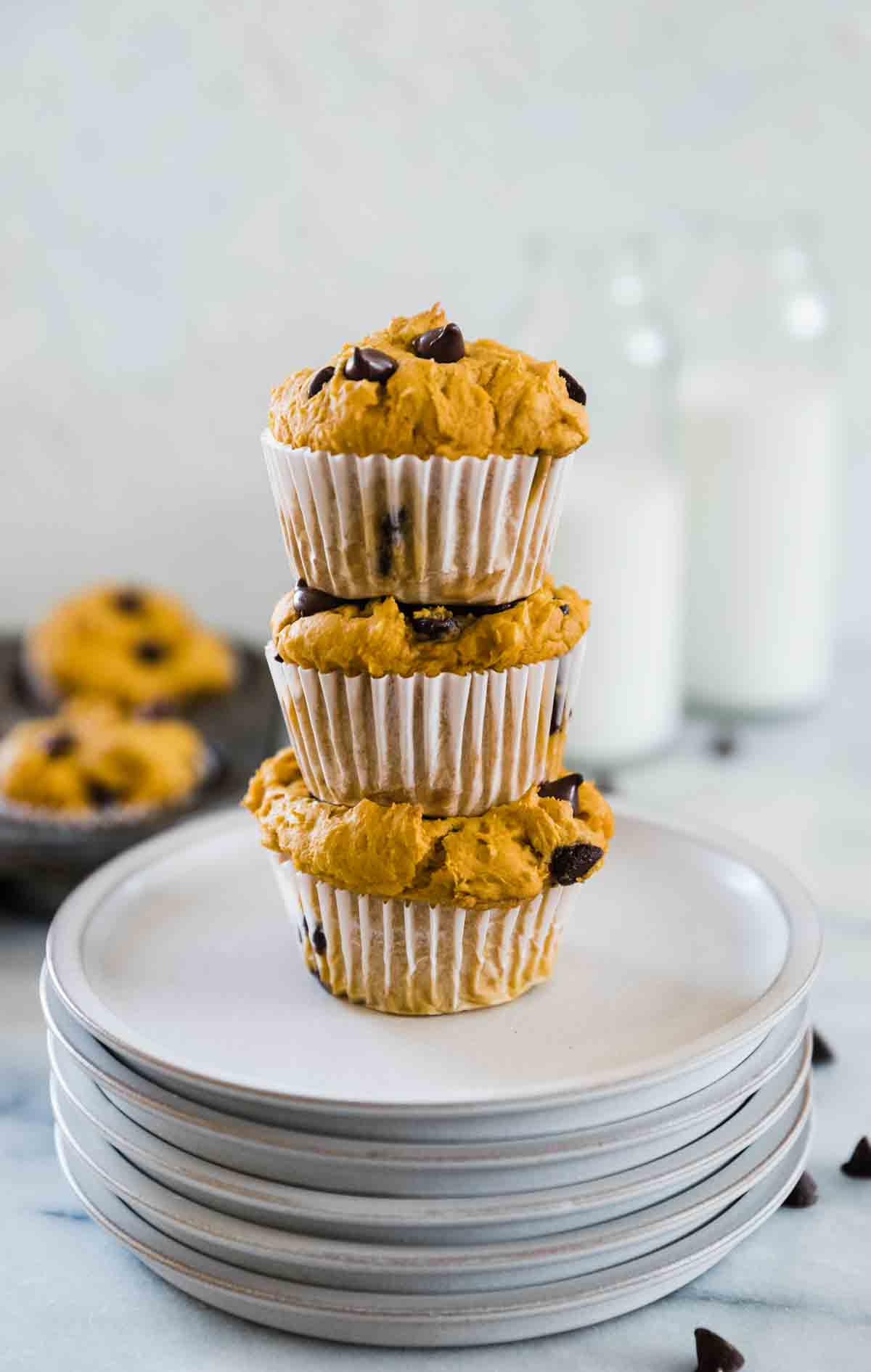 Three cake mix muffins stacked on a plate. There are glasses of milk in the background.