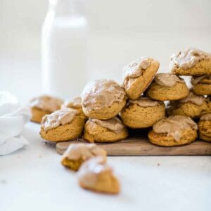 Soft pumpkin cookies on a wooden board. There is a glass of milk in the background.