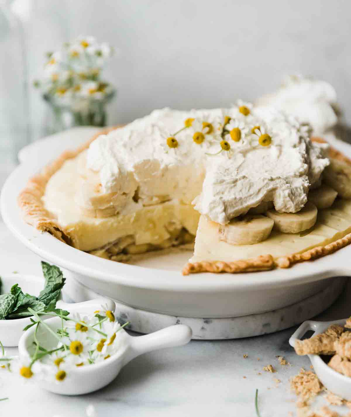 A ¾ shot of easy banana cream pie in a white pie plate. It is garnished with flowers.