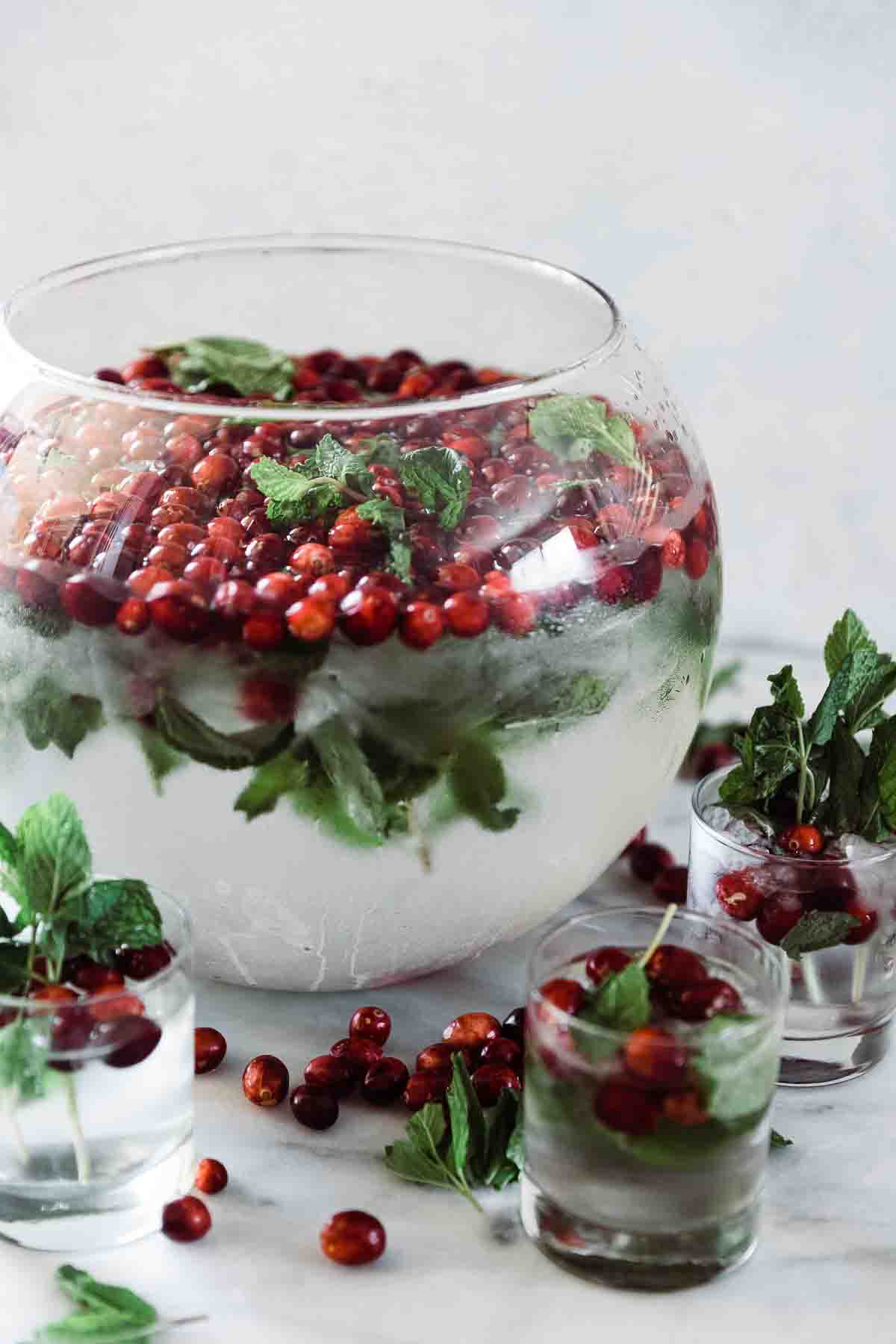 Cranberry mint water in a punch bowl. There are small glasses of water to the side.