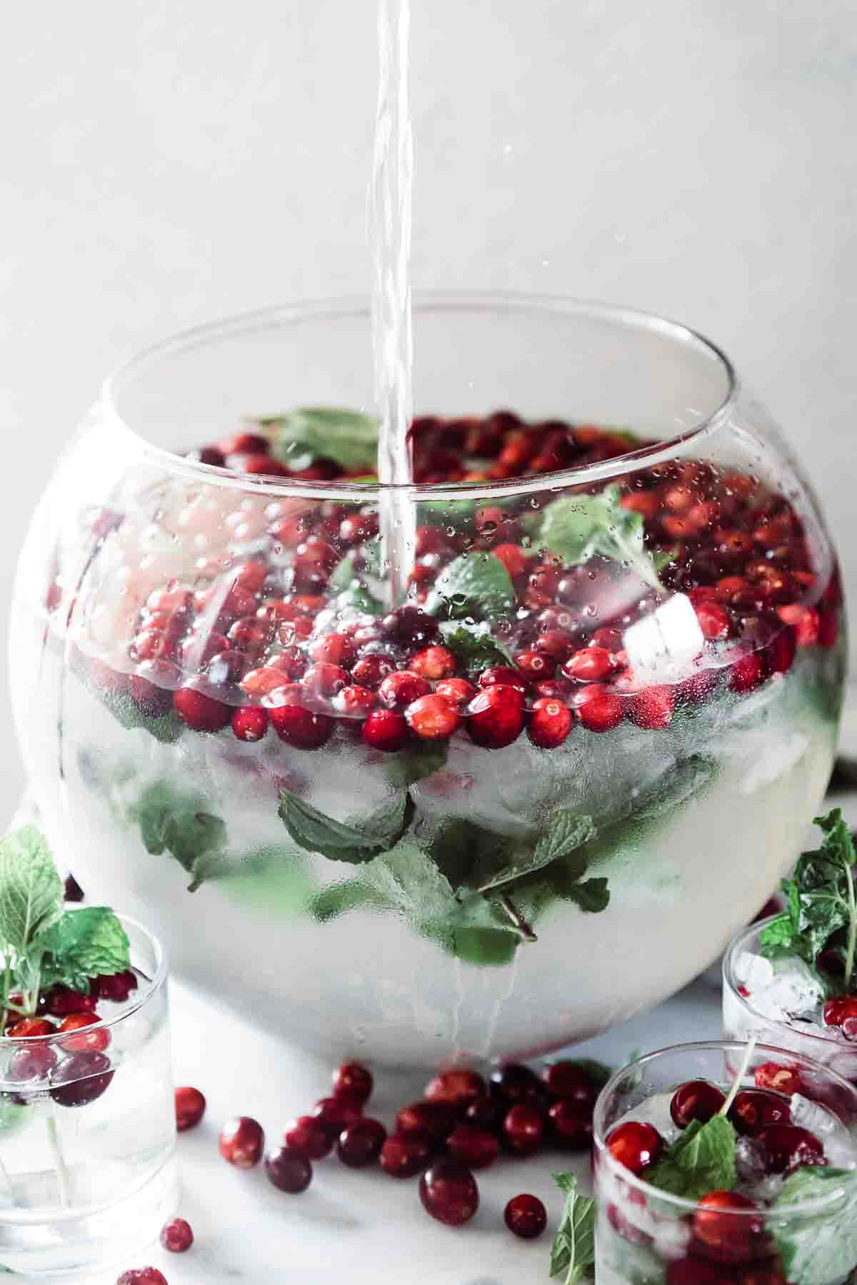 Cranberry mint water in a glass punch bowl. Water is being poured into it.